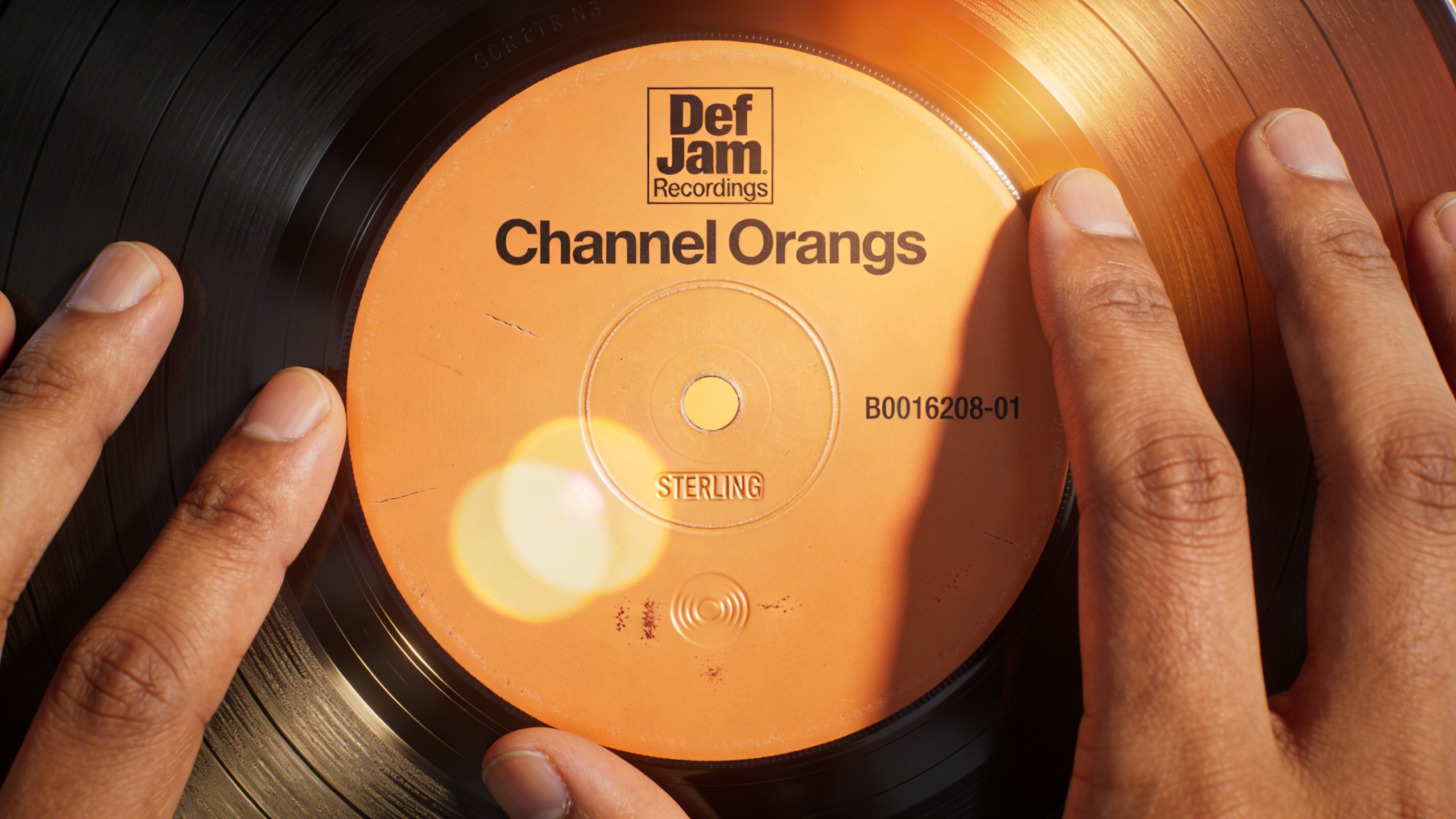 Photorealistic: Close-up of Channel Orange vinyl label showing Def Jam catalog number, warm golden hour lighting, vinyl surface reflecting light, authentic pressing details visible, collector's hands 
